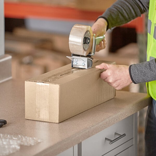 A person wearing a safety vest using a tape dispenser to seal a Lavex shipping box.