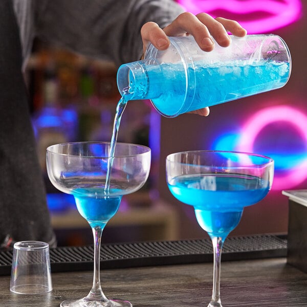 A person using a clear plastic Choice Cobbler cocktail shaker to pour blue liquid into a glass.