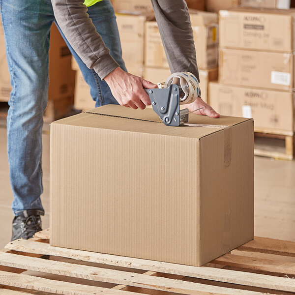 A person using a tape gun to seal a Lavex cardboard shipping box.