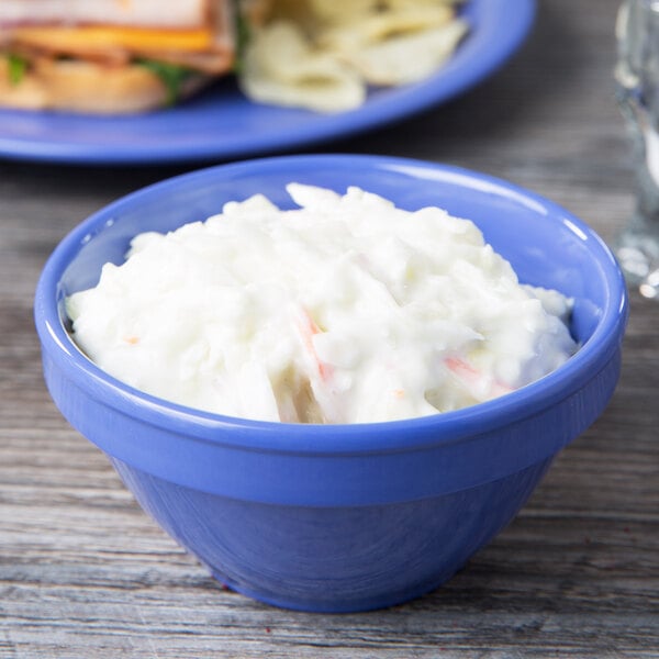 A bowl of coleslaw on a table with a sandwich on a plate.