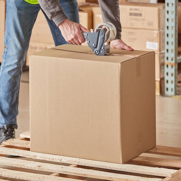 A man in a yellow vest packing a Lavex cardboard shipping box.