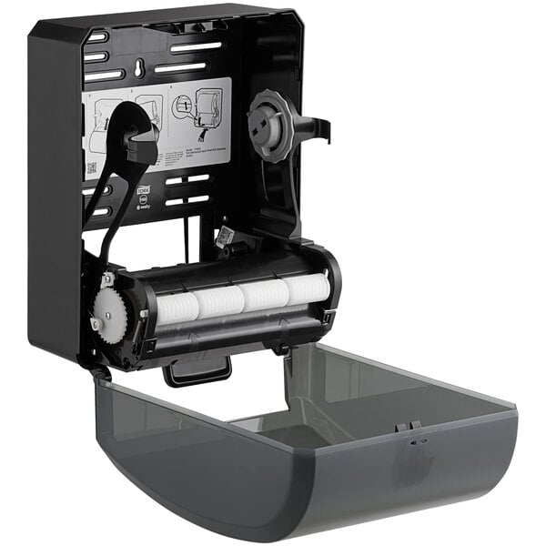 A black Tork mechanical paper towel dispenser with white rollers.