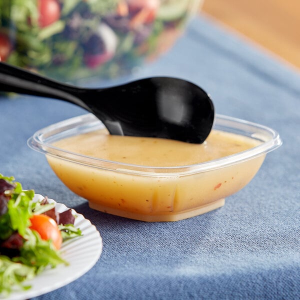 A clear Visions square bowl of salad with a spoon.