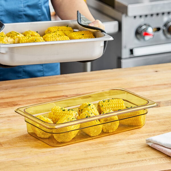 A woman holding a Carlisle amber plastic food pan filled with corn.