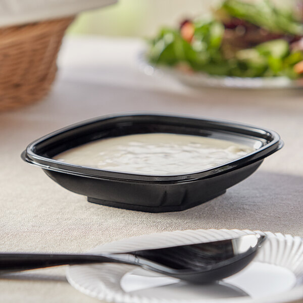 A black Visions plastic catering bowl filled with white liquid on a table.