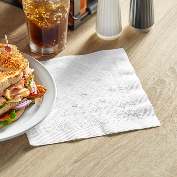 A plate of sandwich and a drink on a Tork white 1/4 fold dinner napkin.