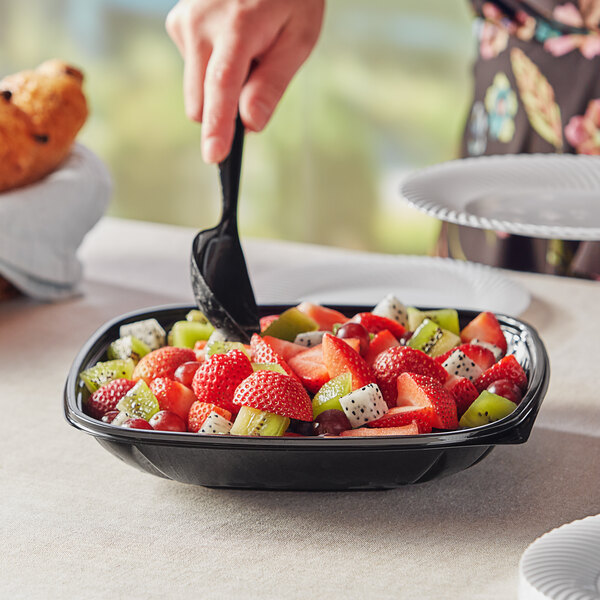 A hand holding a black Visions catering bowl filled with fruit.