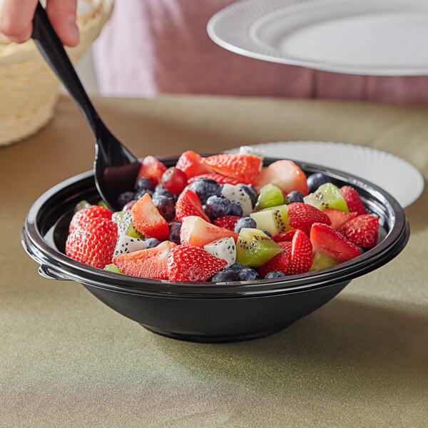 A Visions black plastic bowl filled with fruit salad with a spoon in it.