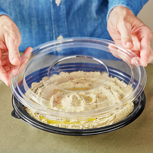 A person holding a Visions clear plastic lid over a bowl of food.