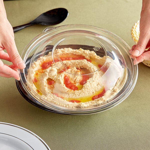 A person holding a Visions clear plastic bowl of hummus with a clear plastic lid.