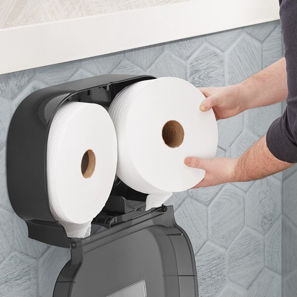 A man holding two Tork jumbo toilet paper rolls.