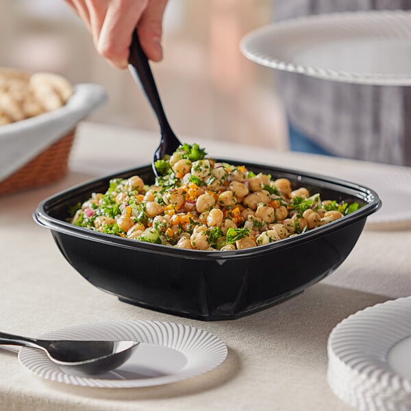 A person holding a spoon over a bowl of food in a Visions black plastic bowl.