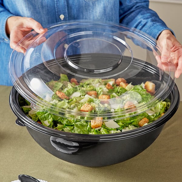 A woman holding a clear plastic lid over a salad bowl.