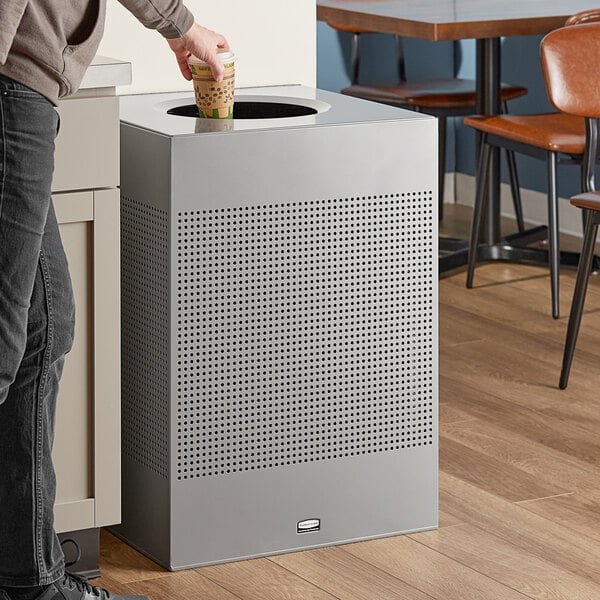 A man in a corporate office cafeteria pours coffee into a Rubbermaid Silhouettes silver metallic steel designer square waste receptacle.