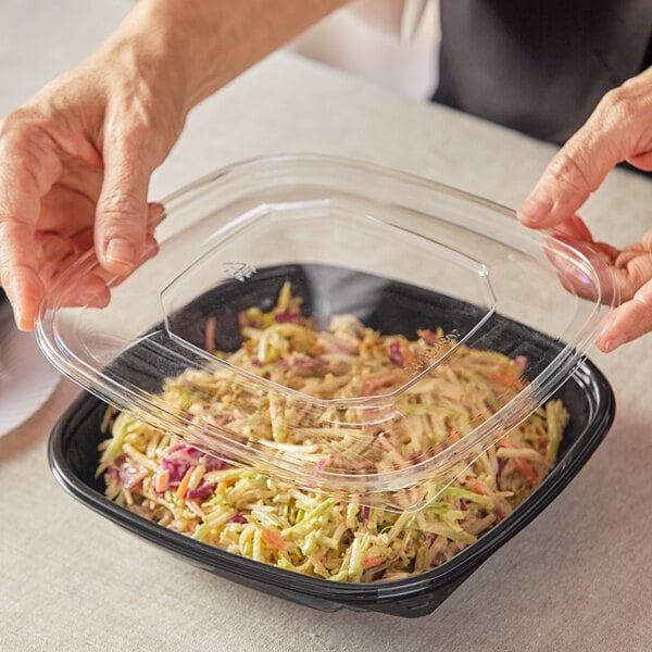 A hand holding a clear plastic container of food.