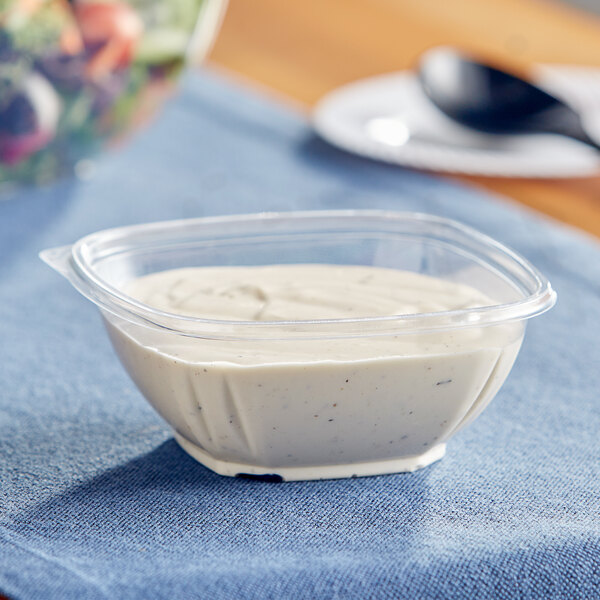 A Visions clear plastic square bowl filled with white sauce.