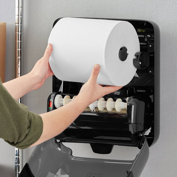 A person holding a roll of Tork Advanced Matic soft white paper towels.