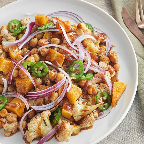 A plate of food with vegetables and a piece of food with Knorr Jamaican Jerk sauce on it with a knife and fork.