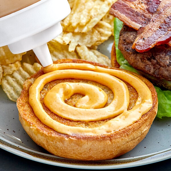 A close-up of a burger with bacon and cheese being drizzled with Hellmann's Spicy Mayonnaise.