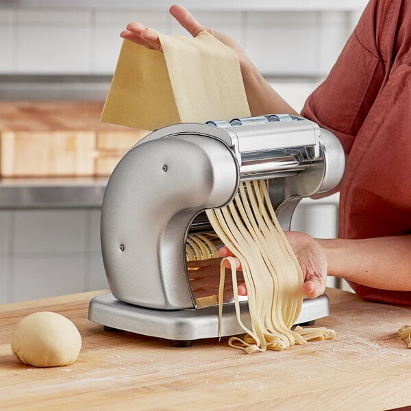 A woman using an Imperia Pasta Presto machine to make pasta with a ball of dough on a table.