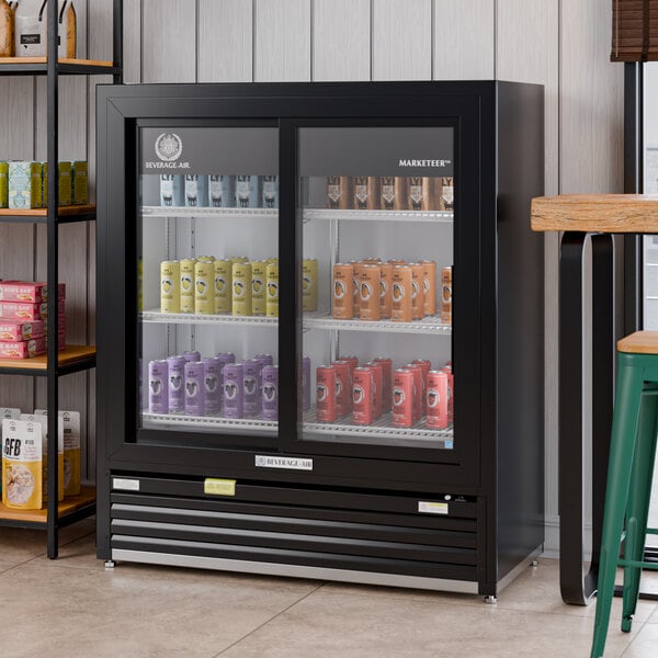 A black refrigerated sliding glass door merchandiser with LED lighting, stocked with assorted canned beverages.