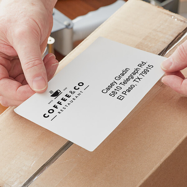 A person's hand holding a Lavex white fanfold label.