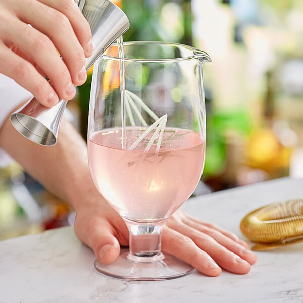 A person using a Barfly footed stirring glass to pour a pink drink.