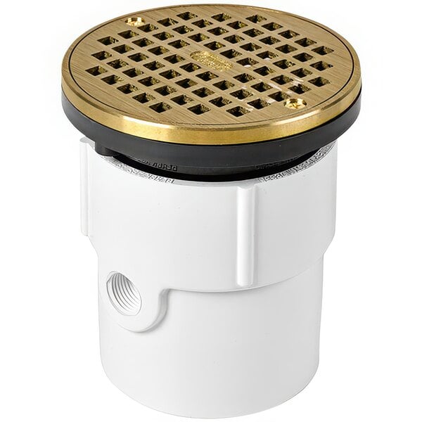 An Oatey PVC floor drain with a brass cover with white and gold accents.