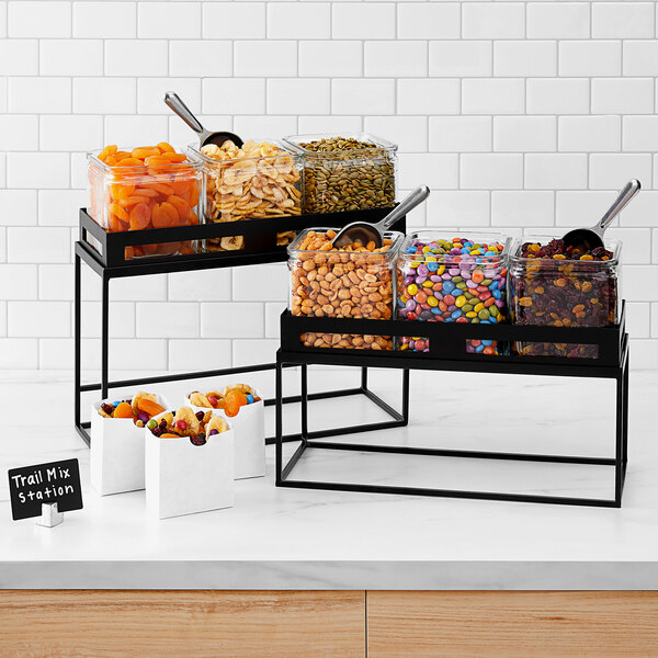 A black metal rectangular riser with food containers on a counter.