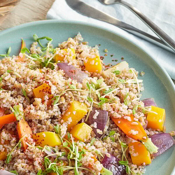 A plate of Bob's Red Mill Whole Grain Red Bulgur Wheat with vegetables and grains on a table next to a fork and knife.