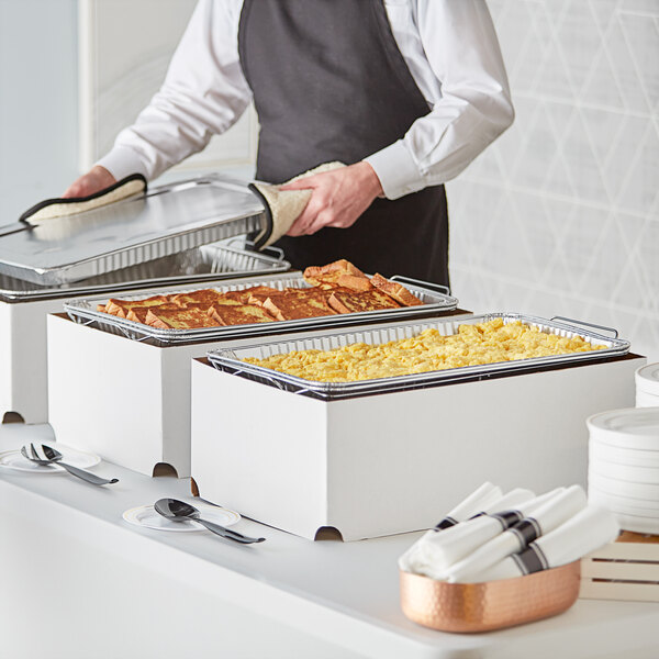 A man in an apron preparing food in a hotel buffet using Choice chafer dishes.