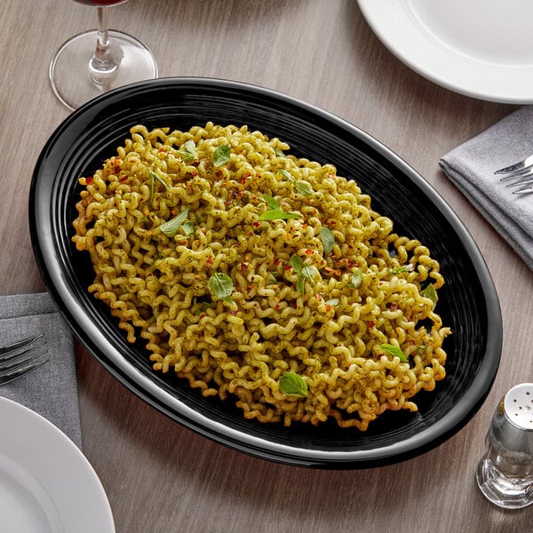 A Tuxton black oval china coupe platter with noodles on a table.