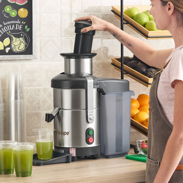 A stainless steel automatic juicer with pulp ejection being used on a kitchen counter.