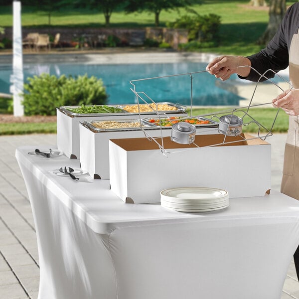 A woman standing next to an outdoor buffet table with a Choice disposable chafer dish kit on it.