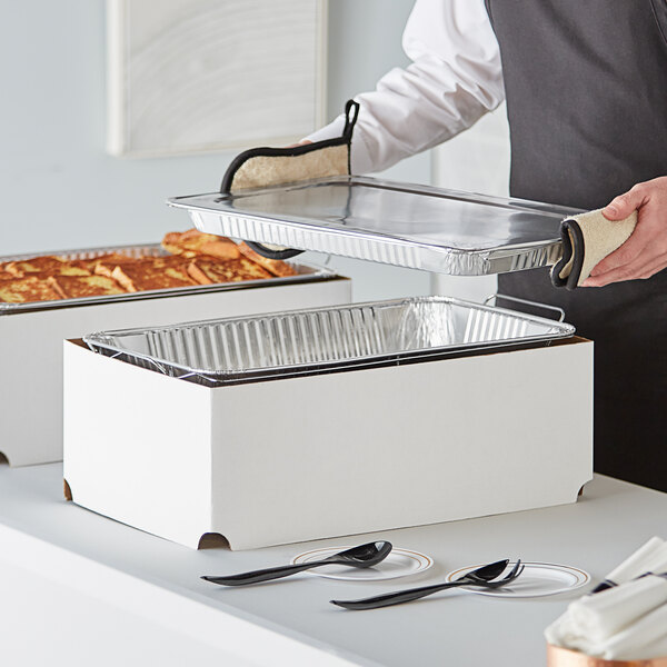 A person holding a white rectangular Choice chafing dish with trays of food in it.