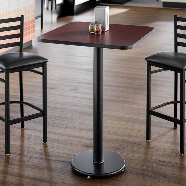 A square laminated table with a reversible cherry and black finish, supported by a single pedestal base.