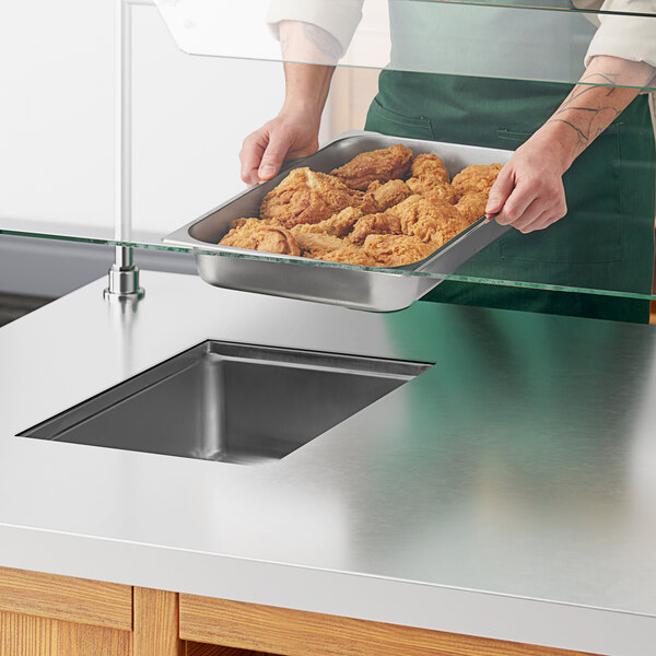 A person holding a tray of fried chicken over a metal drop-in hot food well.