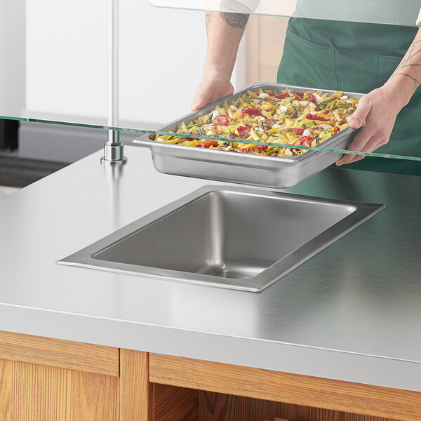 A person holding a tray of food over a drop-in hot food well.