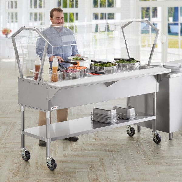 A man standing at a stainless steel ice-cooled food table with clear plastic sneeze guards.