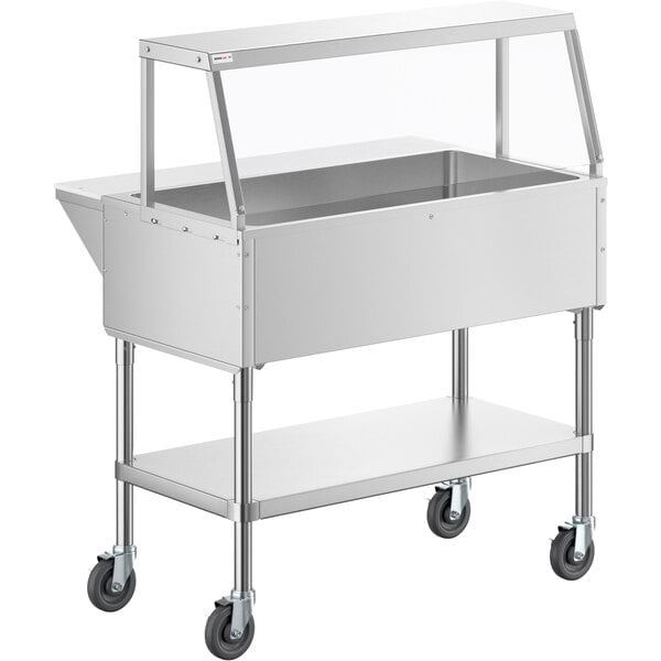A stainless steel ServIt ice-cooled food table on casters with an angled glass sneeze guard.