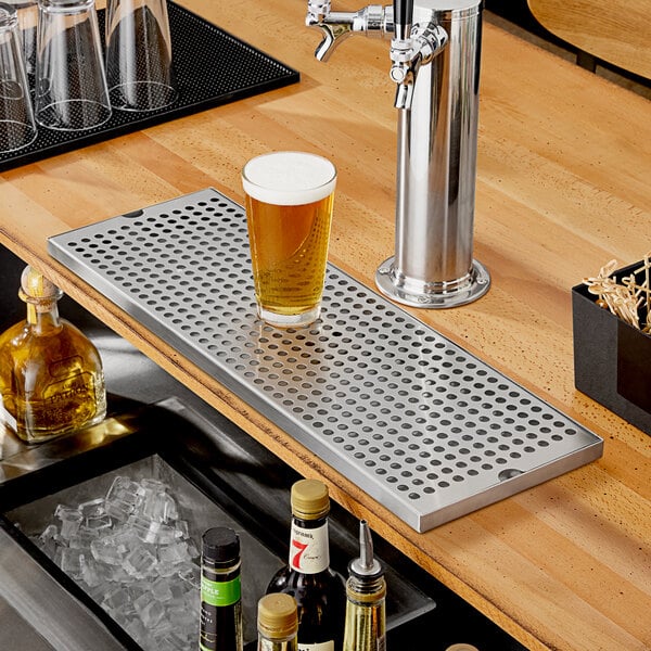 A Regency stainless steel beer drip tray on a bar counter with a glass of beer.