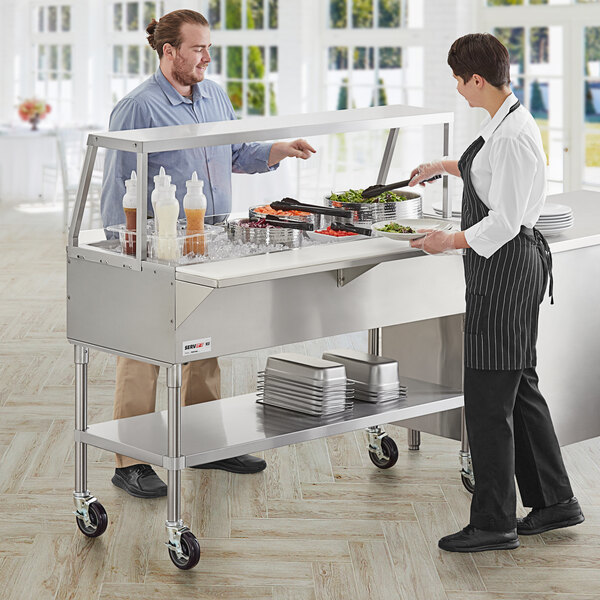 A man and woman standing in front of a ServIt ice-cooled food table with food.