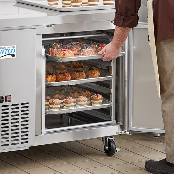 An unassembled aluminum sheet pan rack filled with food in front of a refrigerator.