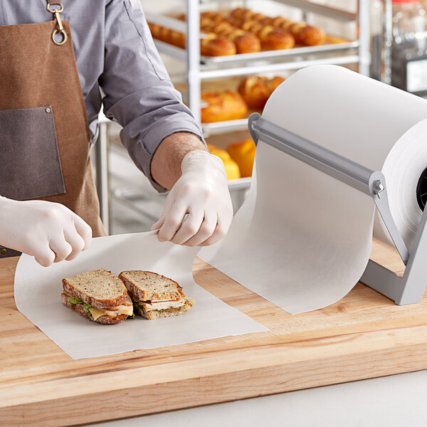 A man in a white apron and gloves using Choice 15" x 1000' Premium Wet Wax Paper to wrap a sandwich.