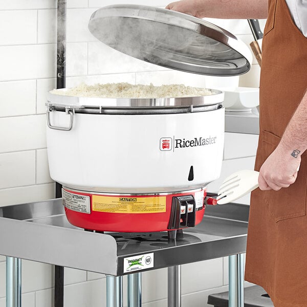 A person using a Town propane gas rice cooker to stir rice in a large pot.