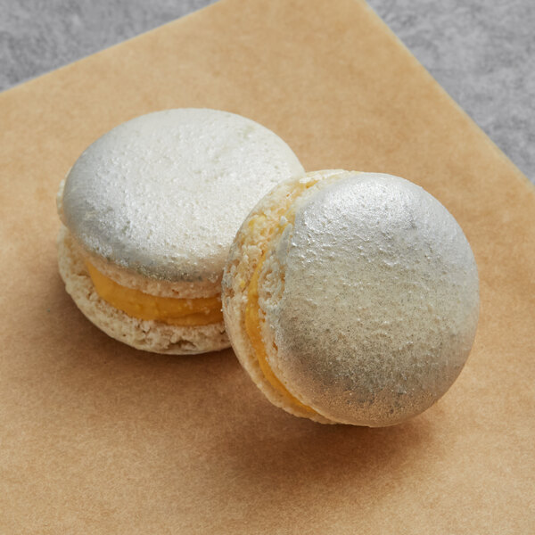 Two Macaron Centrale honey butterscotch macarons on a brown surface.