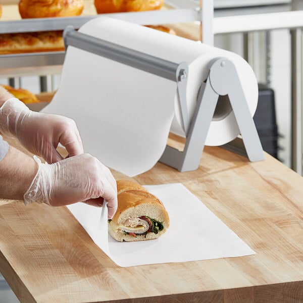A person wearing plastic gloves uses Choice wet wax paper to cut a sandwich.