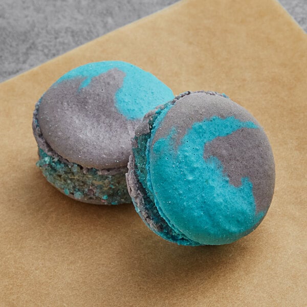 Two blue and grey Macaron Centrale cookies and cream macarons on a brown surface.