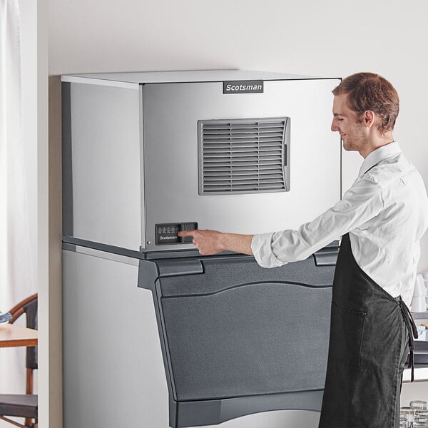 A man in an apron standing next to a Scotsman air cooled medium cube ice machine.