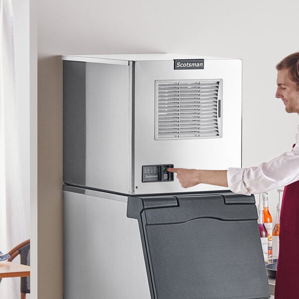 A man in a red apron pressing a button on a Scotsman air cooled small cube ice machine.